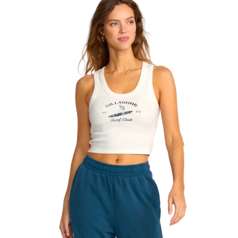 Woman wearing a white tank top with a logo and text, standing against a plain background