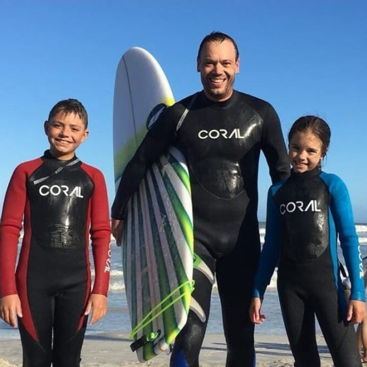 Family of four in wetsuits with a surfboard on a beach