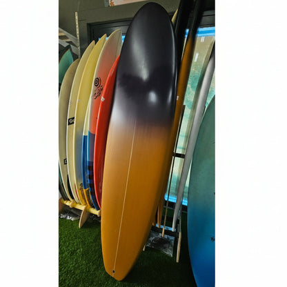 A long surfboard with a black-to-yellow gradient finish leans against a rack of other colorful surfboards in an indoor shop setting.