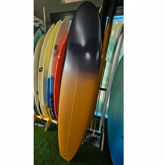 A long surfboard with a black-to-yellow gradient finish leans against a rack of other colorful surfboards in an indoor shop setting.