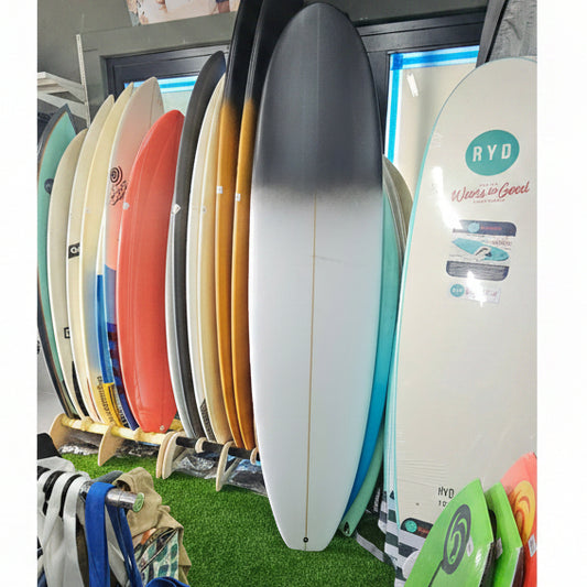 A vertical stack of various surfboards in different colors, including white, blue, yellow, orange, red, and green, displayed on a store shelf next to a green turf floor.