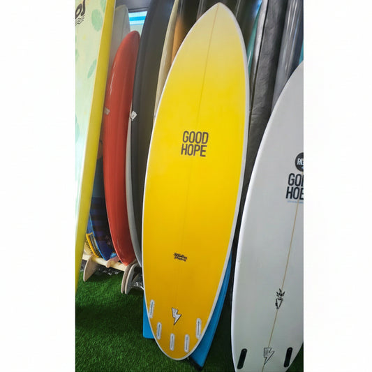 A yellow surfboard with 'GOOD HOPE' printed on the bottom, displayed vertically on a green artificial turf surface alongside other surfboards.