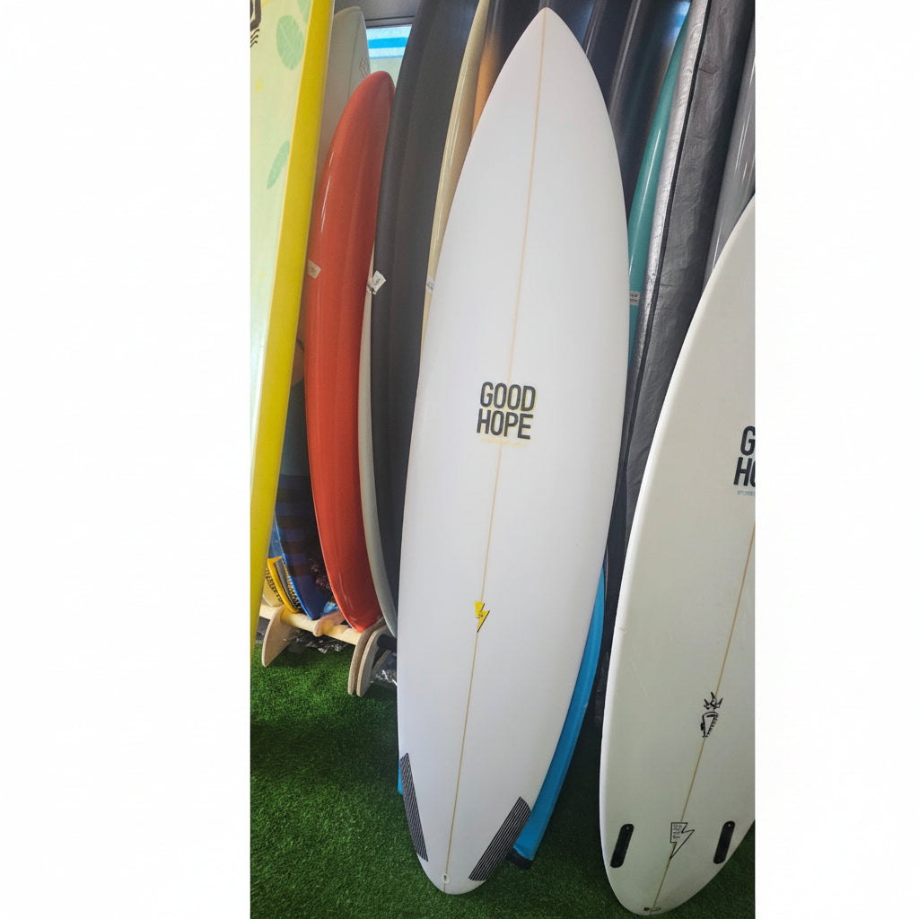 A white surfboard with 'GOOD HOPE' printed in black on the side, displayed among other colorful surfboards on a green artificial turf surface.