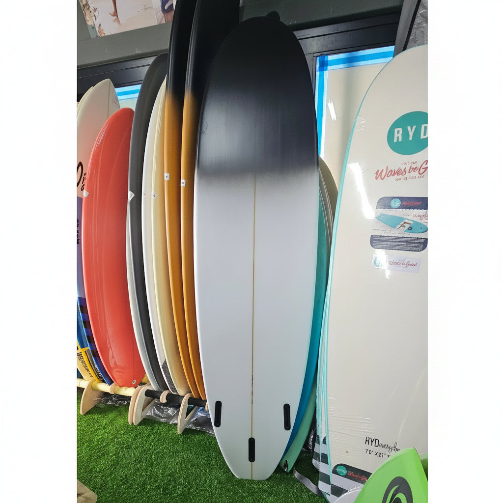 A stack of surfboards in various colors, including black, white, orange, and red, displayed on a stand in a store setting with artificial green turf visible in the background.