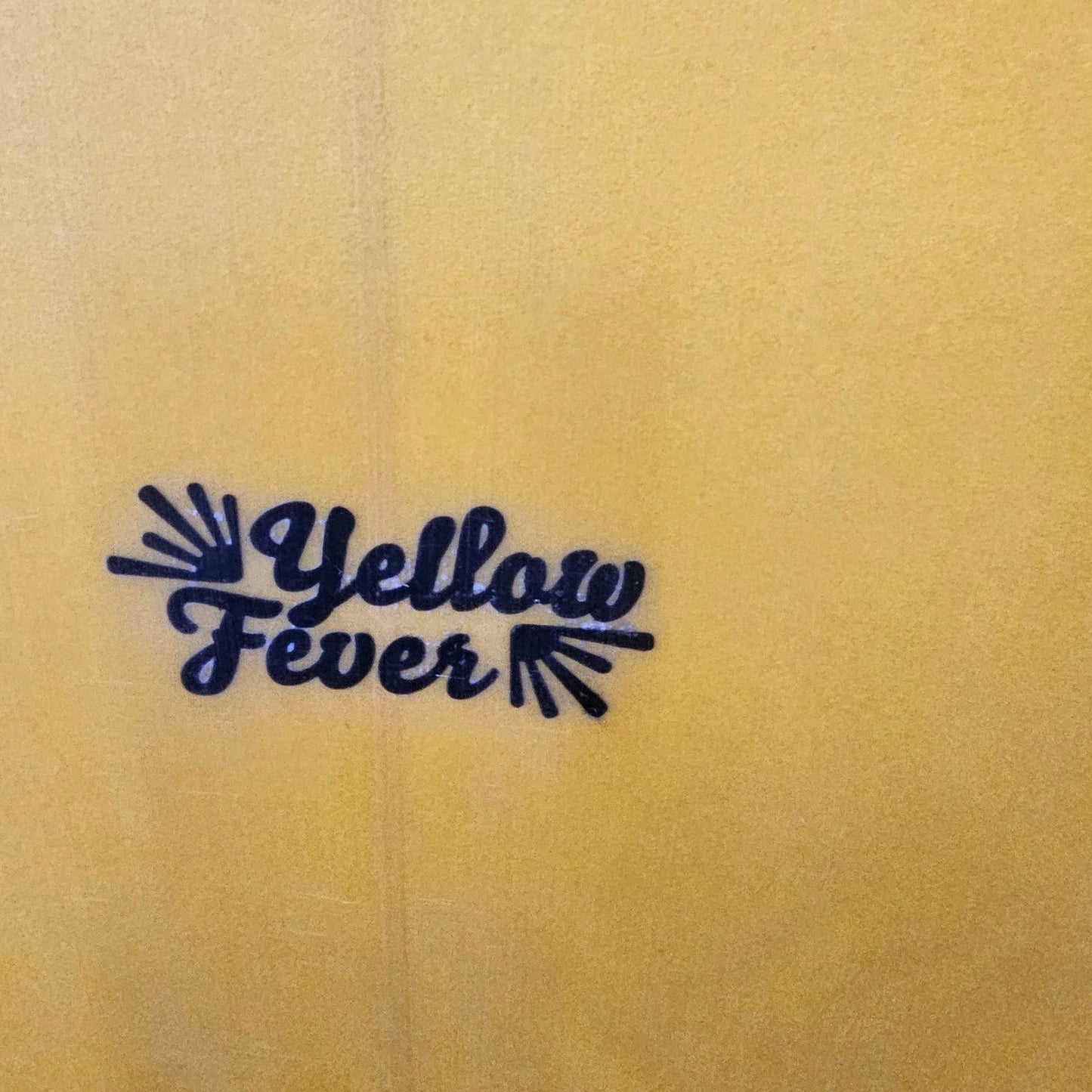 A close-up of a yellow surface with a small dark blue script logo reading 'Yellow Fever' printed near the lower right.