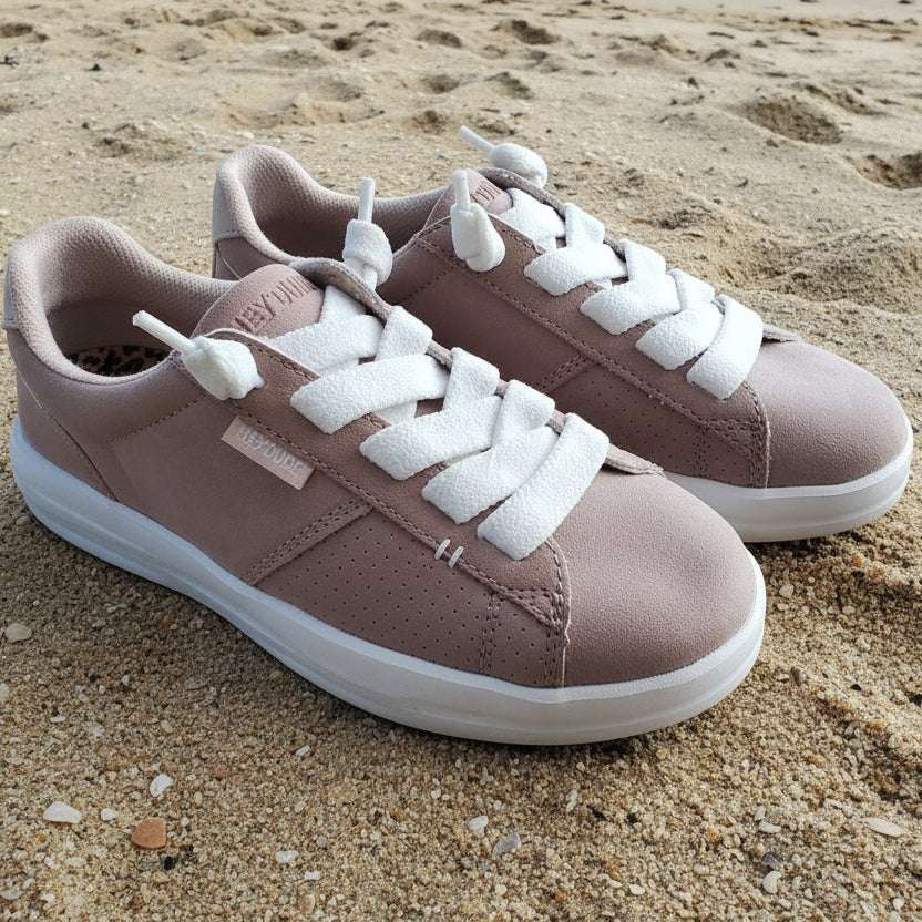 Pair of pink sneakers with white laces on a sandy surface