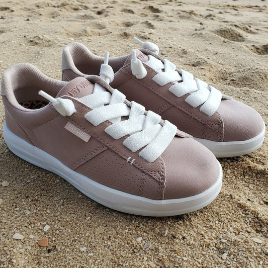 Pair of pink sneakers with white laces on a sandy surface