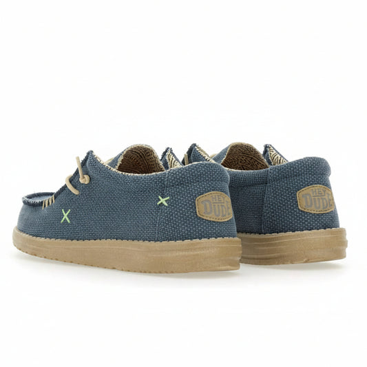 A pair of blue canvas boat shoes with tan soles and laces, shown from a three-quarters angle on a white background.