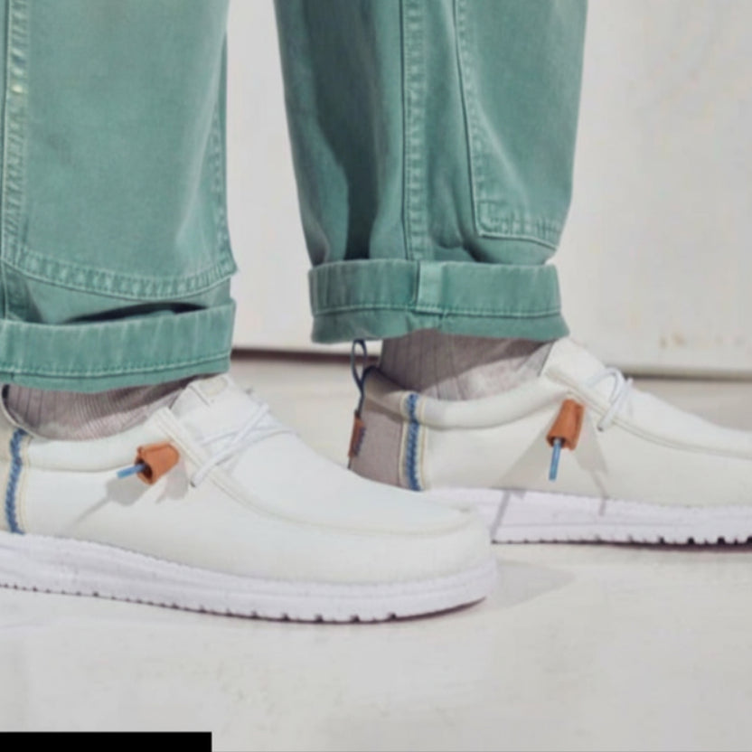 White slip-on shoes worn with light blue jeans on a neutral background
