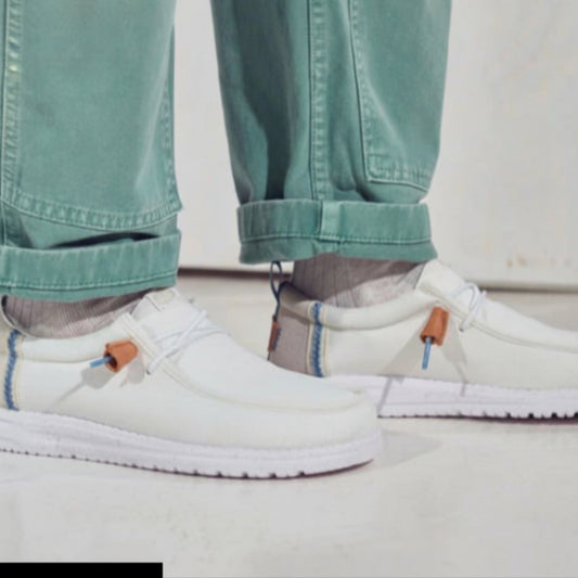 White slip-on shoes worn with light blue jeans on a neutral background