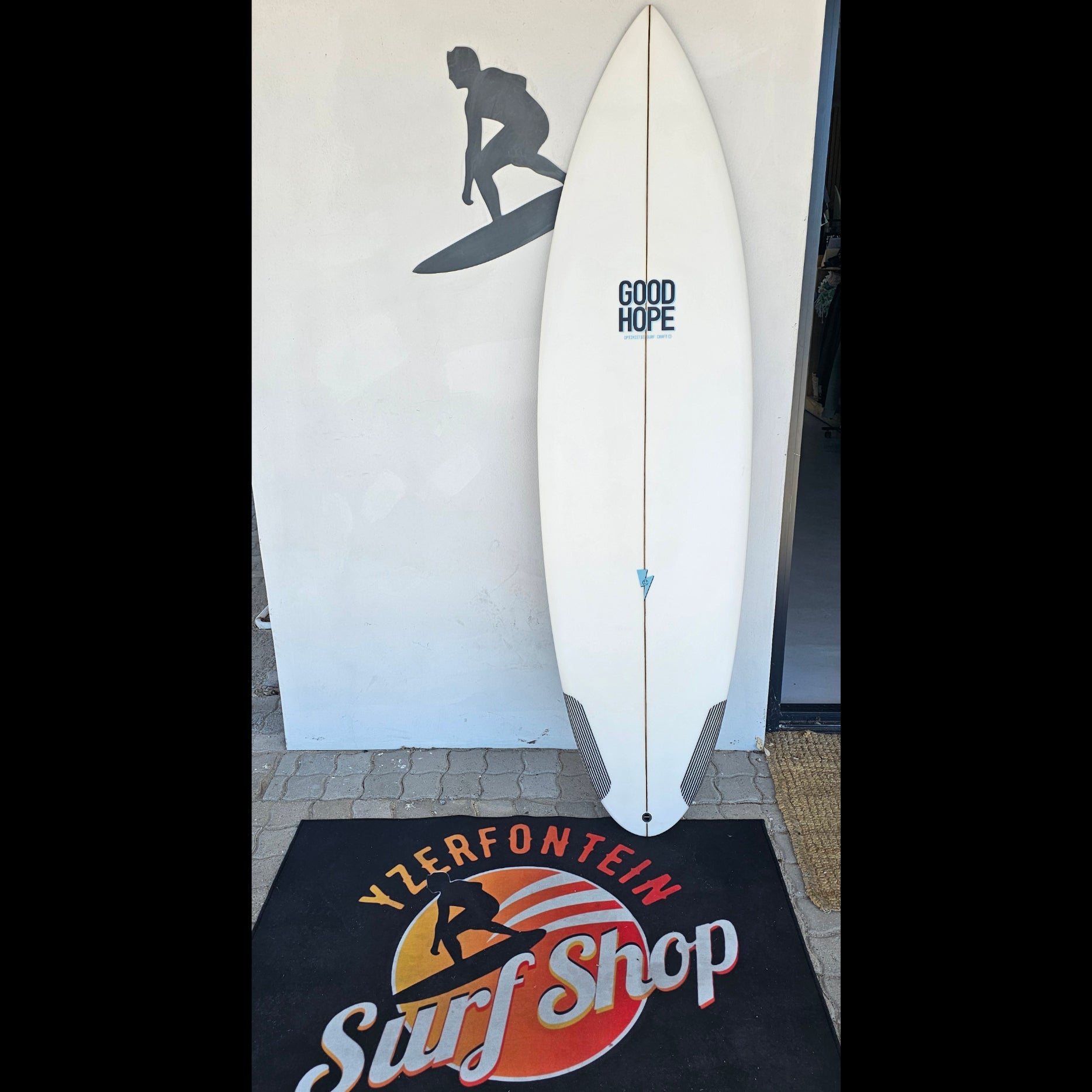 White surfboard with 'Good Hope' branding on a mat with 'Yzerfontein Surf Shop' logo.