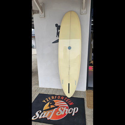 Wooden surfboard leaning against a wall with a surf shop sign in the background