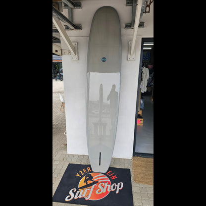 Longboard-style surfboard on a white stand with a surf shop sign in the background.