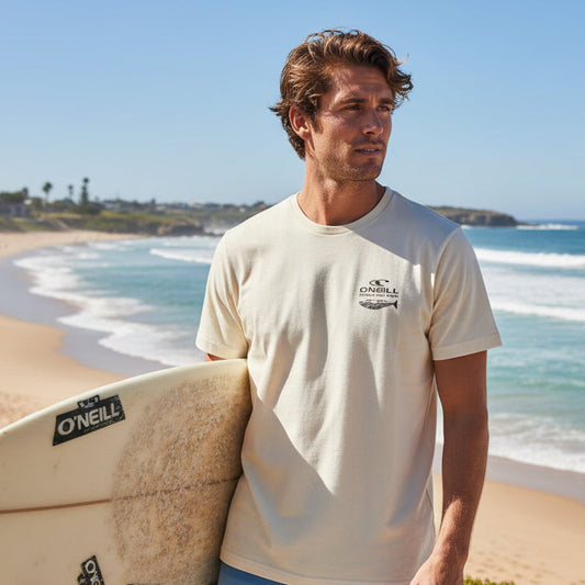 Man holding a surfboard on a beach with ocean and clear sky in the background