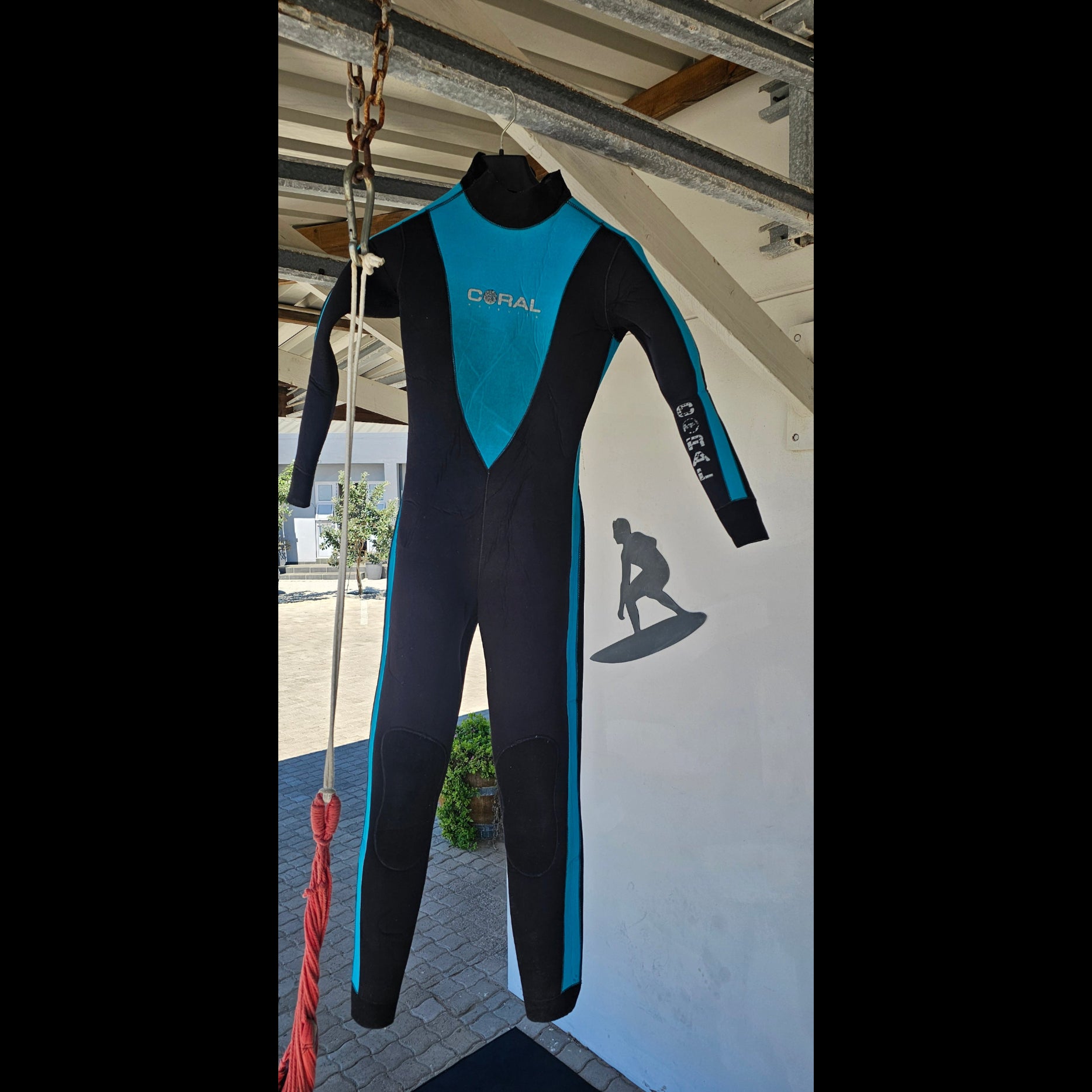 Blue and black wetsuit on a stand with a building and flags in the background