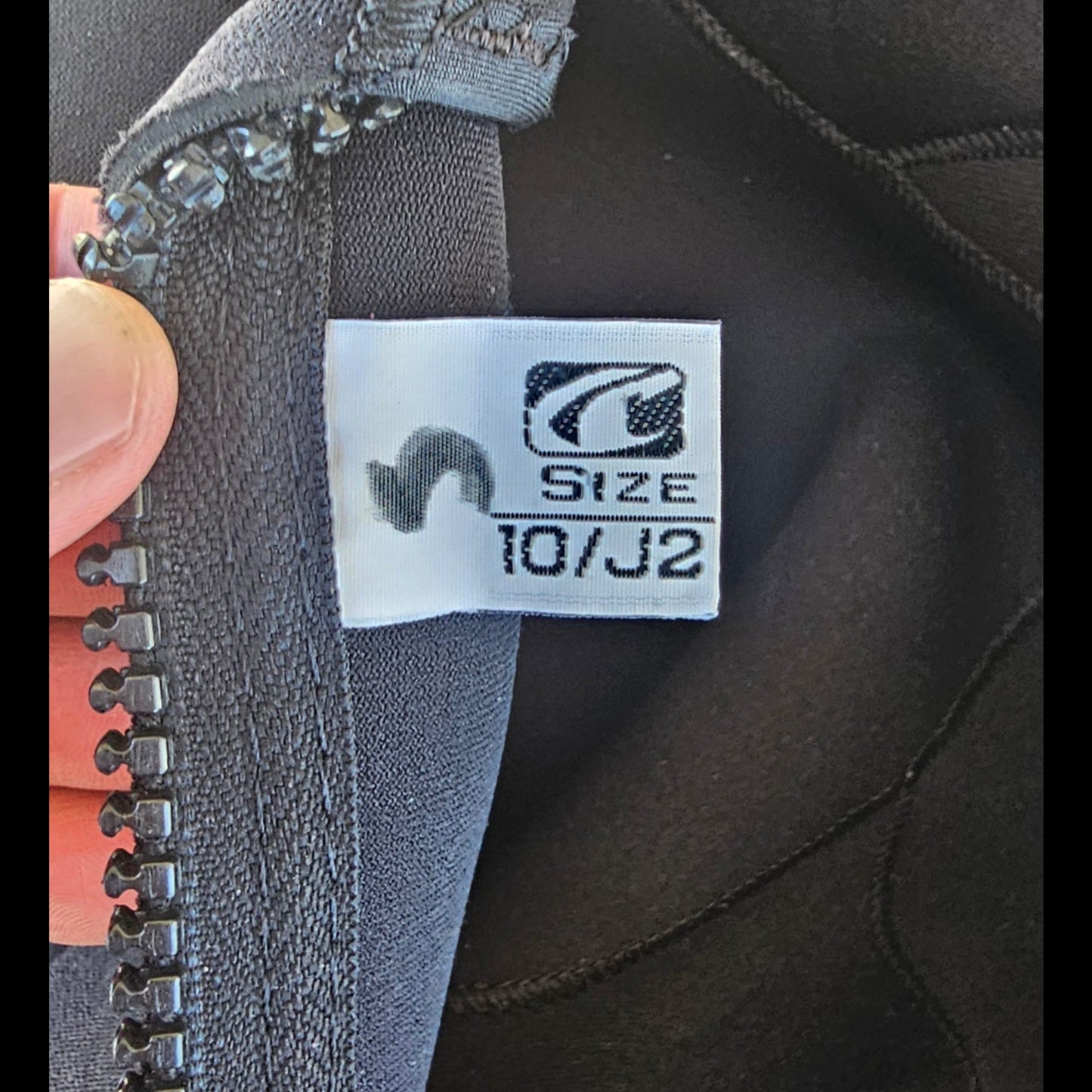 Close-up of a size label on a piece of gray fabric with a zipper.