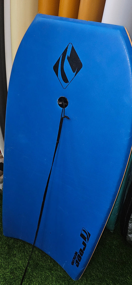 A blue bodyboard with a black leash attached, resting on artificial green turf next to other surfboards.