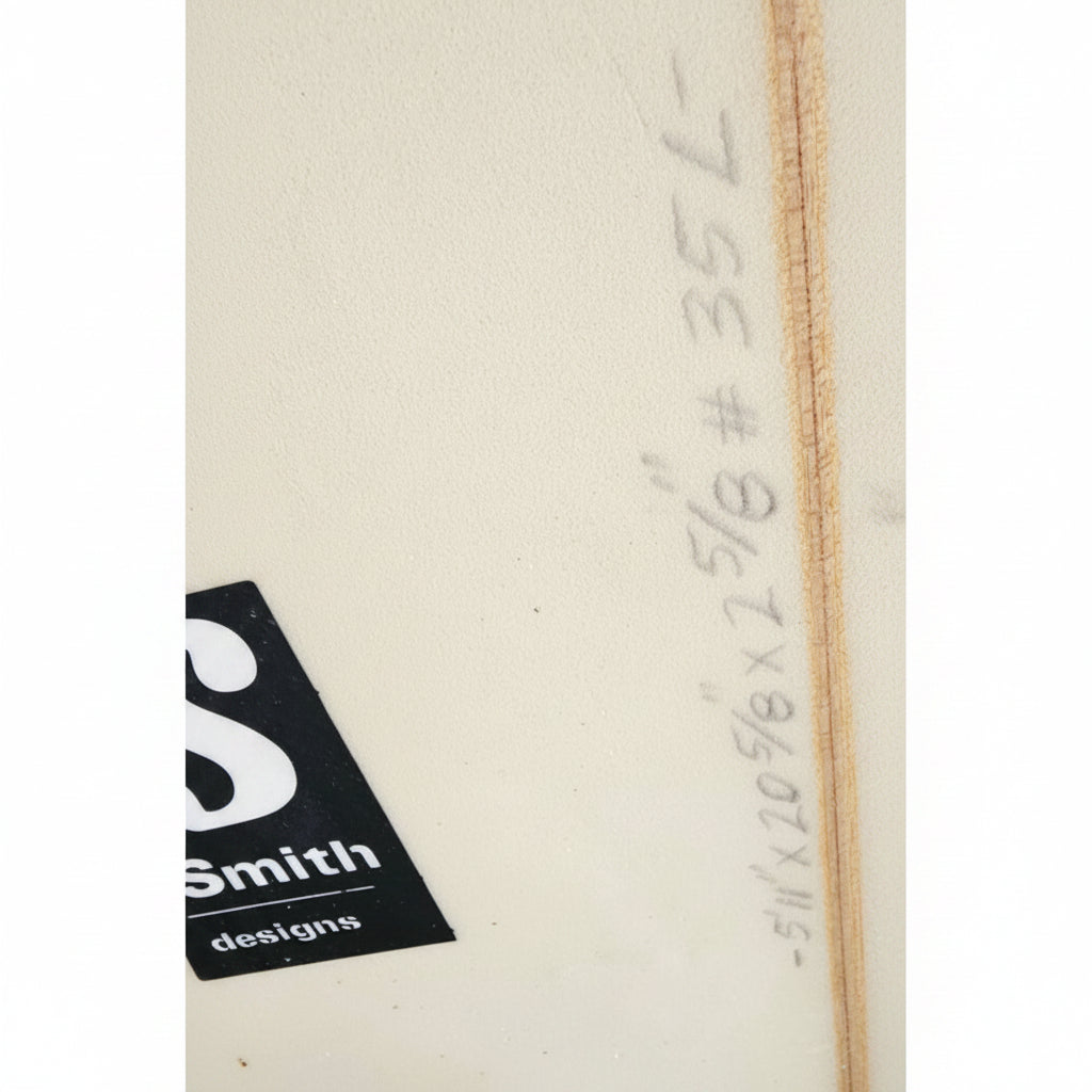 Close-up of a light beige wood panel with handwritten measurements in pencil and a black Smith Designs logo sticker in the lower-left corner.