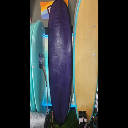 Three surfboards of different colors (purple, blue, and beige) leaning against a wall.