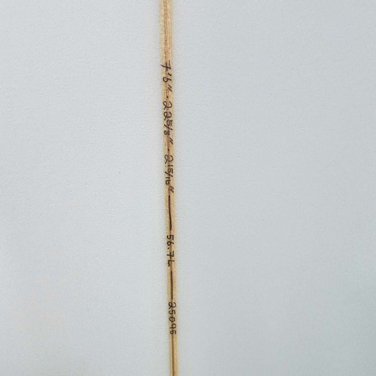 Close-up of a white surfboard showing the center string, printed with wave and distance markings, and a black fin cap on the right side.