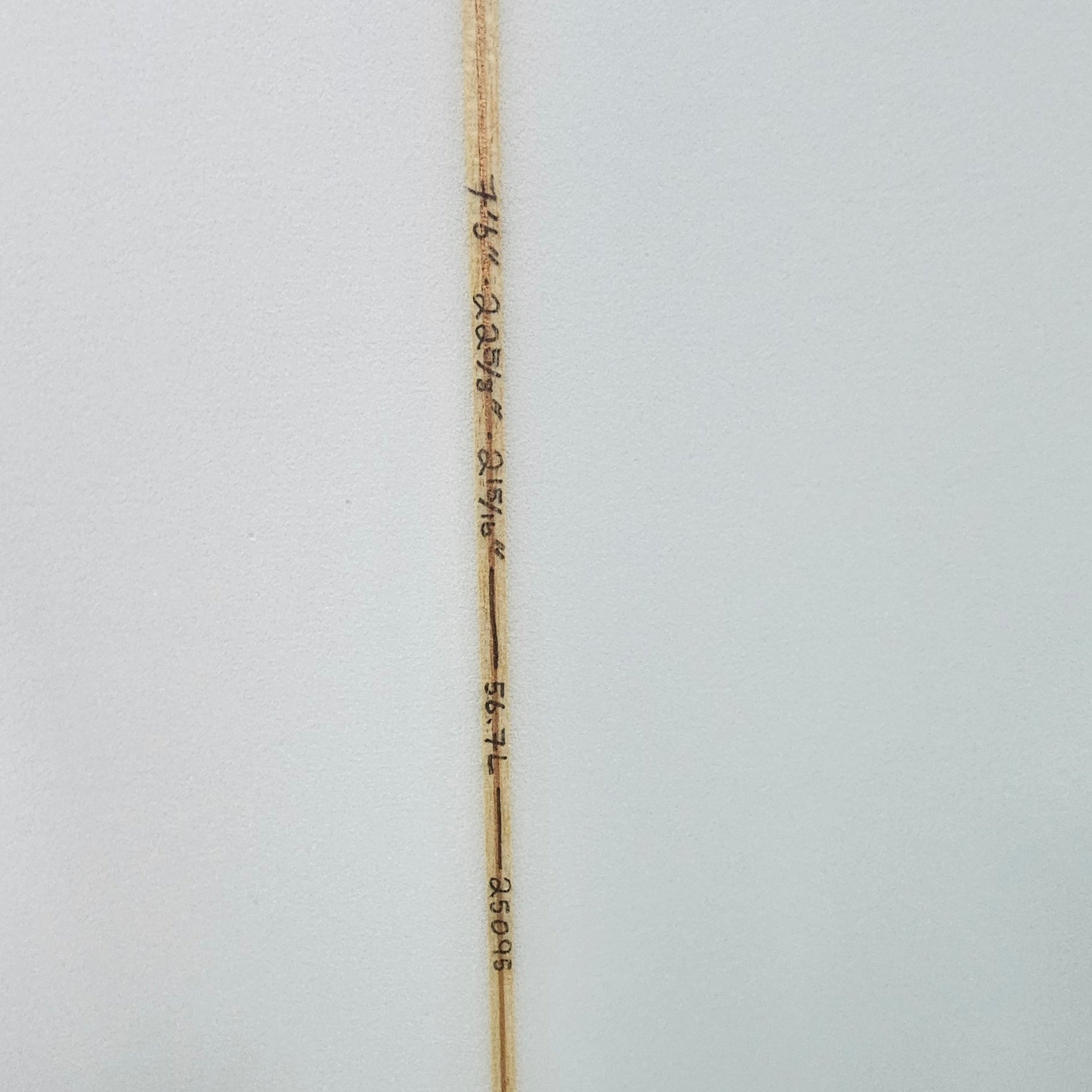 Close-up of a white surfboard showing the center string, printed with wave and distance markings, and a black fin cap on the right side.