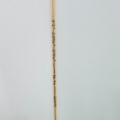 Close-up of a white surfboard showing the center string, printed with wave and distance markings, and a black fin cap on the right side.