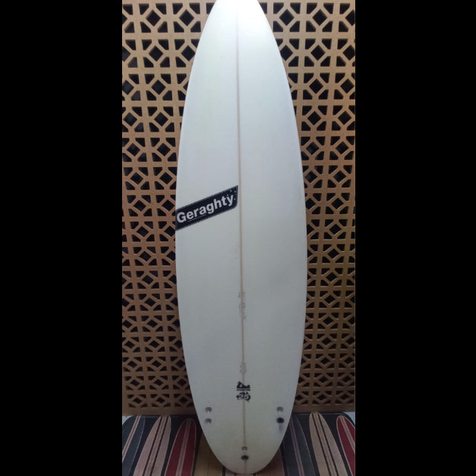 White surfboard with 'Geraghty' branding against a patterned wall.