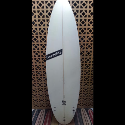 White surfboard with 'Geraghty' branding against a patterned wall.